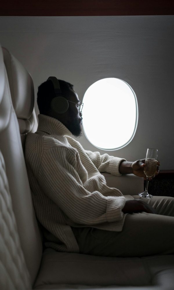 Adult man enjoying a glass of wine while sitting by the airplane window.